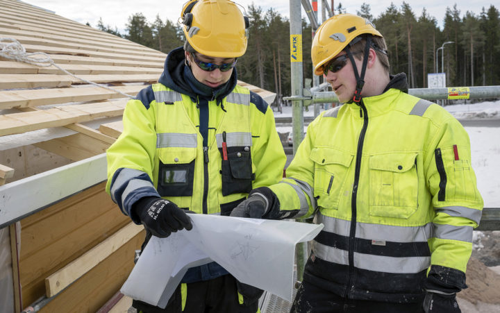 Kaksi rakennusmiestä lukee rakennuspiirustuksia.