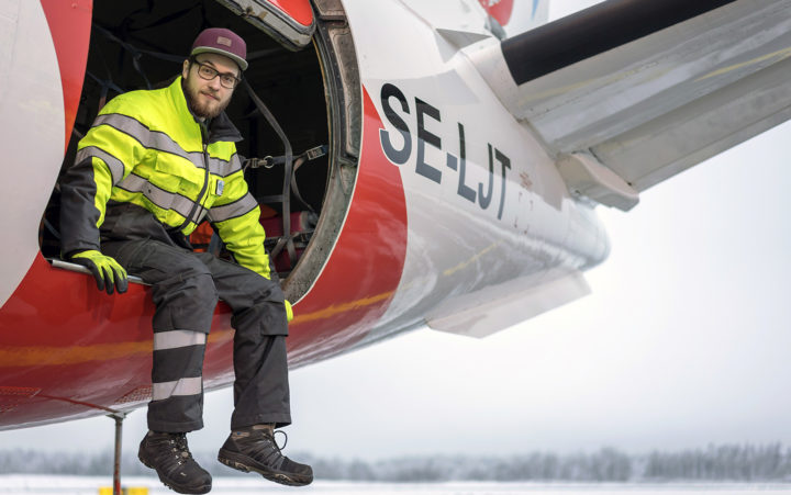 Lentokenttätyöntekijä istuu lentokoneen rahtiaukossa.