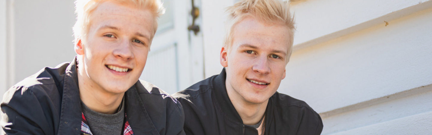 Two blond-haired young men are sitting on the stairs and smiling at the camera