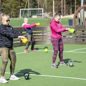 Ryhmä naisia seisoo tekonurmikentällä ja heiluttaa kahvakuulia.