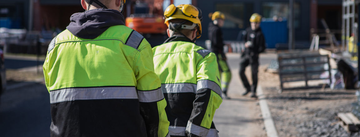 Kaksi keltaisiin kypäriin ja huomiotakkeihin pukeutunutta henkilöä kantaa välissään laastisaavia kohti rakenteilla olevaa taloa.