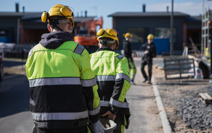 Kaksi keltaisiin kypäriin ja huomiotakkeihin pukeutunutta henkilöä kantaa välissään laastisaavia kohti rakenteilla olevaa taloa.