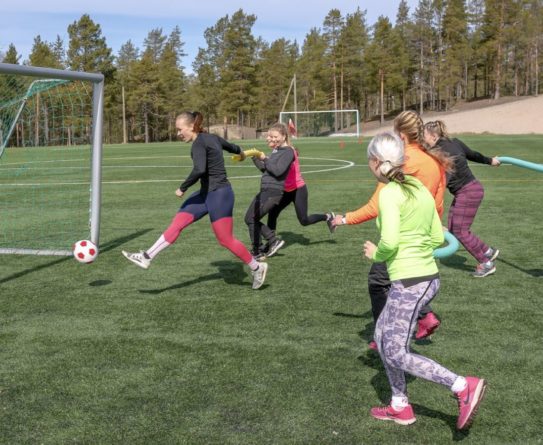 Joukko naisia pelaa nurmikentällä jalkapalloa.