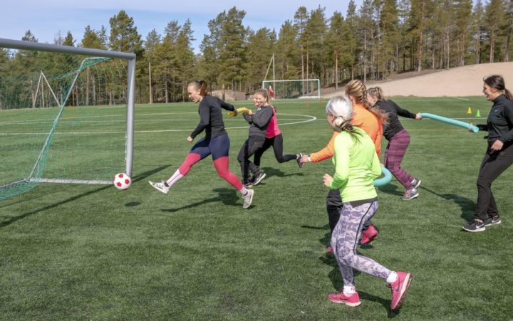 Joukko naisia pelaa nurmikentällä jalkapalloa.