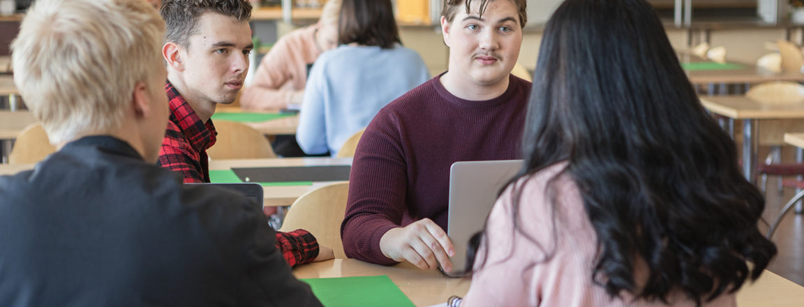 Neljä nuorta opiskelijaa istuu pöydän ääressä. Yhdellä on edessään kannettava tietokone.