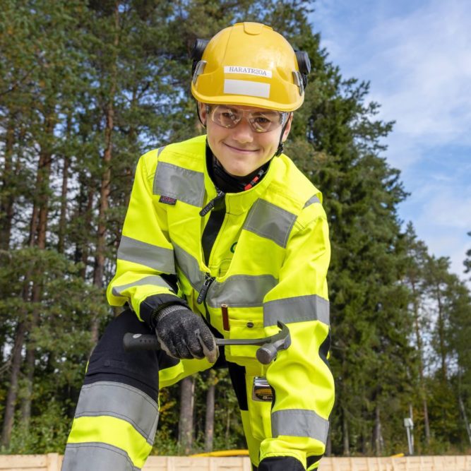 Keltaisiin työvaatteisiin ja kypärään pukeutunut mies pitää vasaraa kädessään.