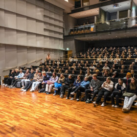 OSAOn konserttisalissa liiketoiminnan opiskelijat istuvat katsomossa ja seuraavat katsomon edessä tapahtuvaa ohjelmaa, jossa henkilö puhuu mikrofoniin.