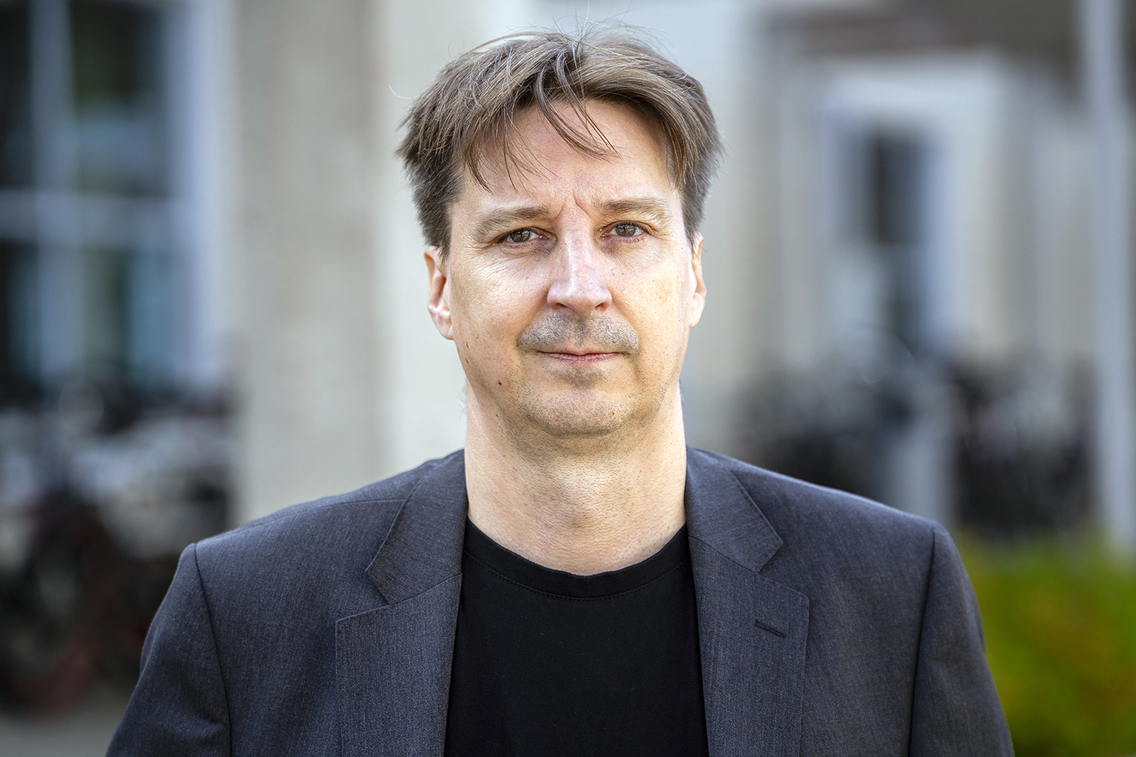 Jouni Juntunen pictured in the courtyard of the University of Oulu wearing a black t-shirt and a dark gray suit jacket.